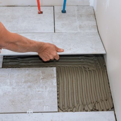 Home construction working with placing ceramic floor tiles over position over adhesive